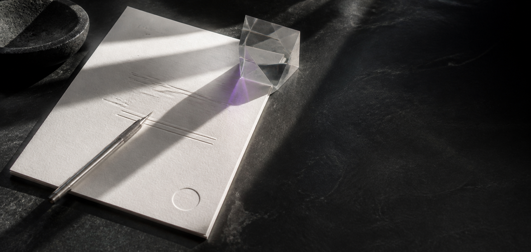 An archival sheet, precision stylus and optical glass prism on dark stone